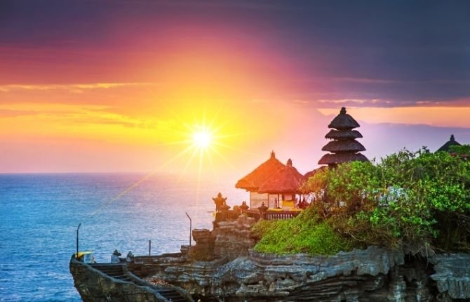 Tanah Lot sea temple on its rock silhouetted against a golden sunset on Bali's west coast
